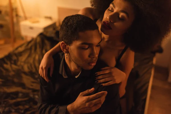Young african american woman with closed eyes embracing shoulders of boyfriend sitting on bed at home — Stock Photo