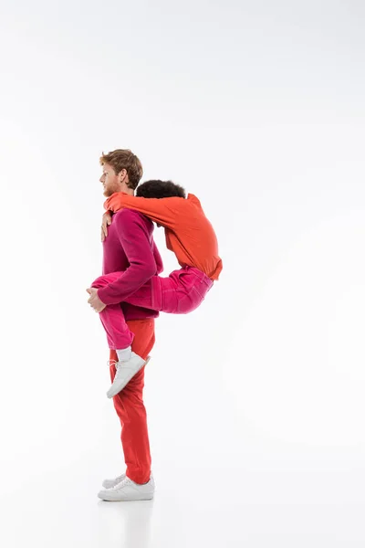 Side view of man in magenta color clothes piggybacking african american woman while showing p letter with bodies on white — Stock Photo