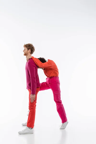 Side view of multiethnic couple in magenta color clothes showing R letter on white background — Stock Photo