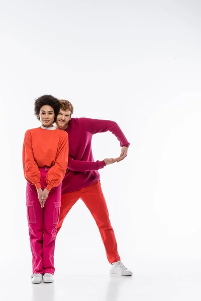 Cheerful and multiethnic couple in magenta color clothes showing R letter on white background — Stock Photo