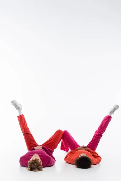 Interracial couple in magenta color clothes lying on floor and showing w letter with legs on white background — Stock Photo