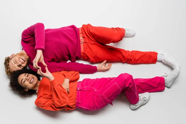 Top view of happy redhead man and curly african american woman in magenta color clothes showing heart with hands on white — Stock Photo