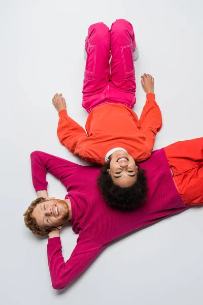 Top view of cheerful redhead man and happy african american woman in magenta color clothes lying on white — Foto stock