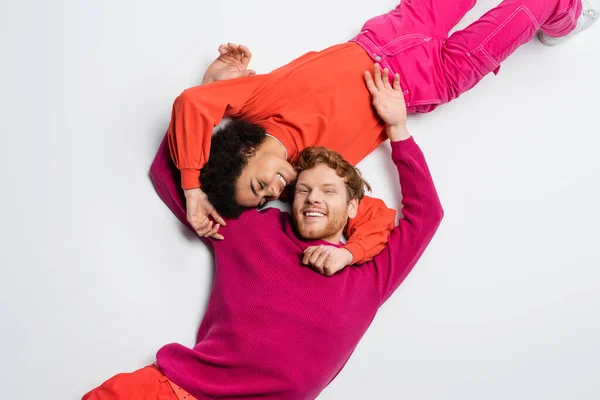 Top view of happy redhead man and curly african american woman in magenta color clothes hugging each other on white - foto de stock