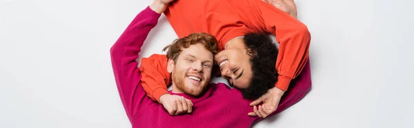 Top view of happy redhead man and cheerful african american woman hugging each other on white, banner — Stock Photo