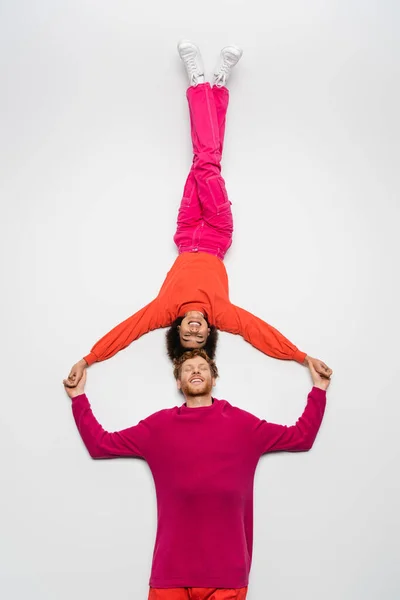 Top view of happy redhead man and positive african american woman in magenta color clothes lying on white — Stock Photo