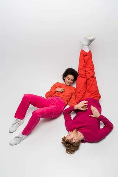 High angle view of happy redhead man and curly african american woman in magenta color clothes on white - foto de stock