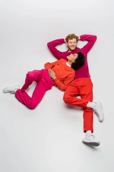 Top view of happy african american woman in magenta color clothes resting with redhead man on white — Stock Photo