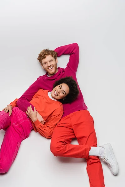 Top view of cheerful african american woman resting with redhead man in magenta color clothes on white — Stock Photo