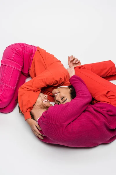 Cheerful african american woman hugging with happy man in magenta color clothes on white — Stock Photo