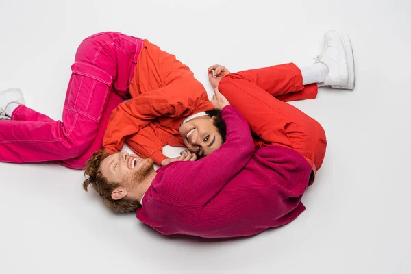 High angle view of smiling african american woman lying with redhead man in magenta color clothes on white — Foto stock