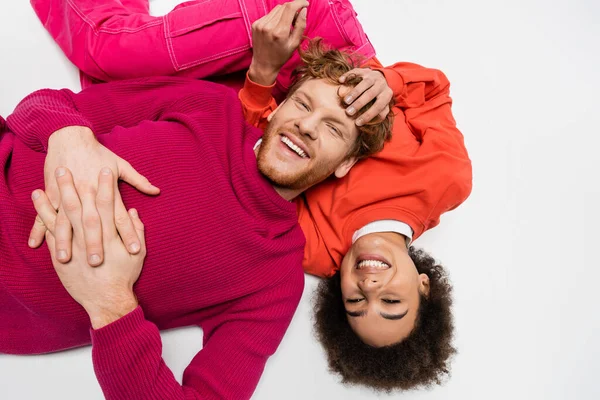 Top view of positive african american woman lying with redhead man in magenta color clothes on white — Stock Photo