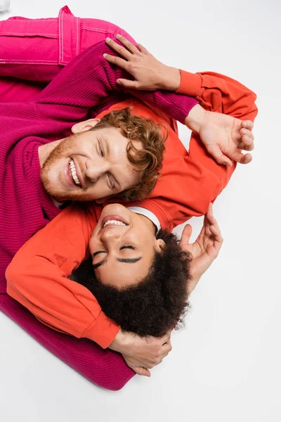 Top view of positive african american woman lying with smiling man in magenta color sweatshirt on white — Photo de stock