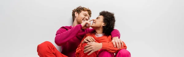 Happy man toughing nose of african american woman in magenta color clothes on grey, banner — Stock Photo
