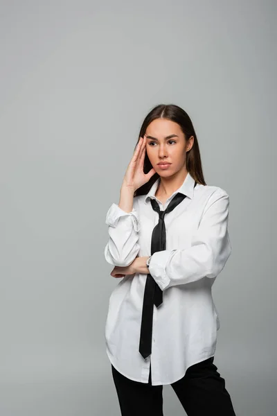 Pensive and brunette woman in white shirt and tie looking away isolated on grey — Stockfoto