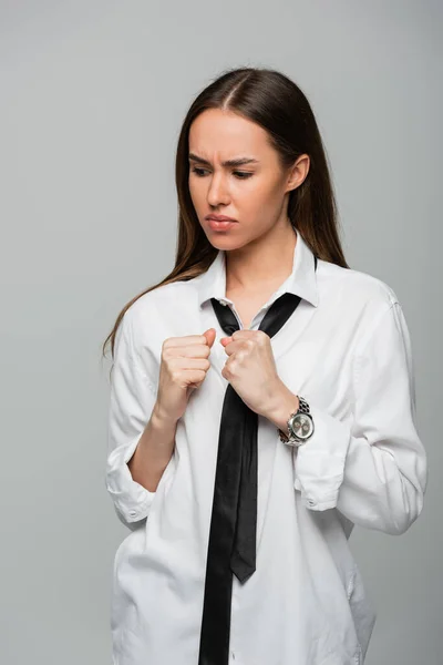 Tenso e morena mulher em camisa branca e gravata olhando para relógio de pulso isolado em cinza — Fotografia de Stock