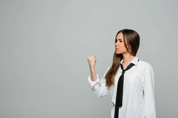 Angry young woman in white shirt and tie showing clenched fist isolated on grey — Stock Photo