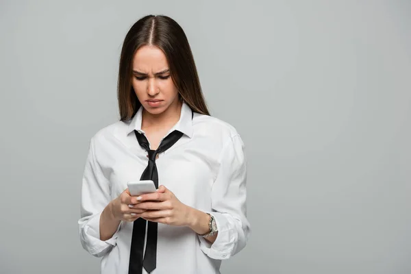 Young woman in white shirt and tie messaging on smartphone isolated on grey — Stock Photo