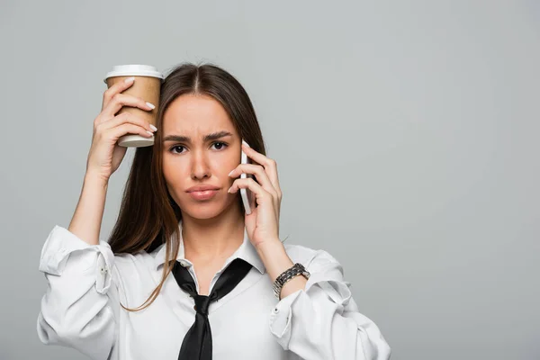 Young woman in white shirt with tie talking on smartphone and holding paper cup with coffee to go isolated on grey — Stock Photo