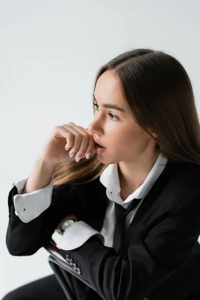 Overhead view of dreamy woman with long hair sitting in suit and leaning on wooden chair back isolated on grey — Stockfoto