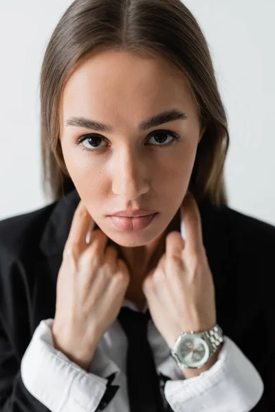 Portrait of pretty and brunette woman in black suit with tie looking at camera isolated on grey — Stock Photo