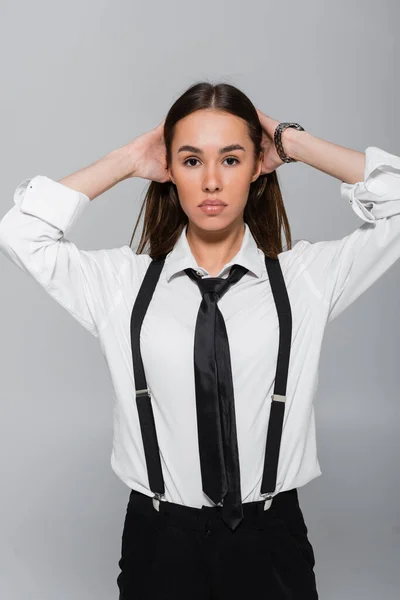 Brünette junge Frau in schwarzen Hosen und Hosenträgern schaut vereinzelt in die Kamera auf grau — Stockfoto