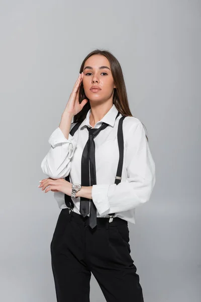 Brunette young woman in black pants with suspenders looking at camera isolated on grey — Photo de stock