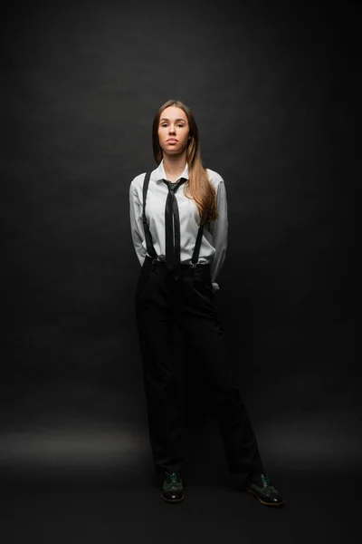 Full length of brunette woman in formal wear with suspenders standing on black — Stock Photo
