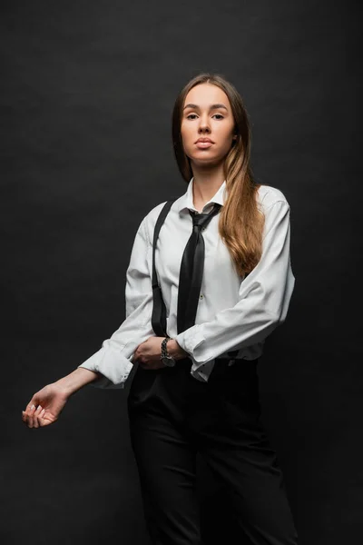 Brunette woman with long hair standing in formal wear with suspenders while posing on black — Foto stock