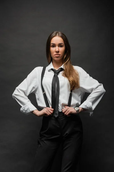 Brunette woman with long hair standing in formal wear with hands on hips on black - foto de stock