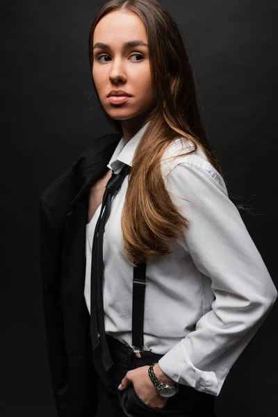 Young woman with brunette long hair standing in suit and holding blazer on black — Stock Photo
