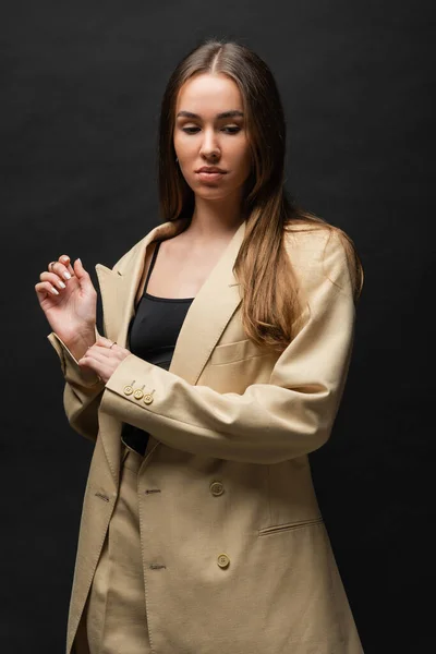 Brunette young woman in beige suit standing and looking away on black — Fotografia de Stock