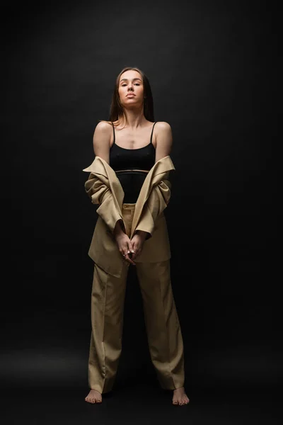 Full length of barefoot young woman in beige suit standing on black — Stock Photo