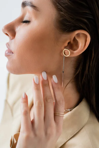 Close up view of pretty young woman with closed eyes and golden jewelry posing isolated on grey — Foto stock