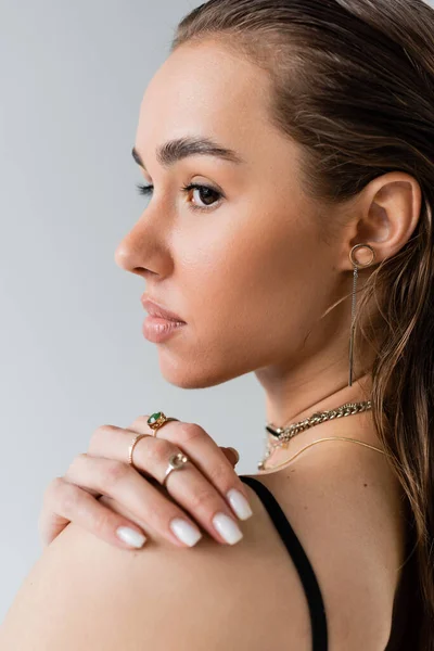 Portrait of brunette woman in black top looking away while touching shoulder isolated on grey — Stock Photo