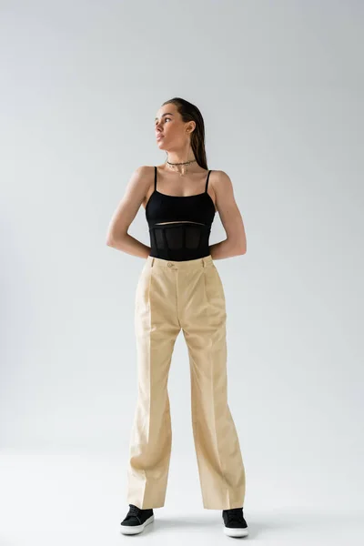 Full length of pretty model in beige pants and black top looking away on grey — Stock Photo