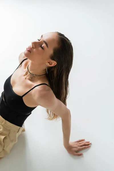 High angle view of brunette woman in beige pants and black top posing on grey — Foto stock