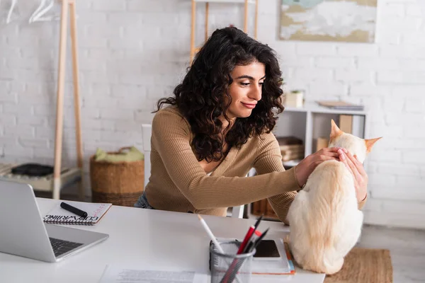 Positive copywriter petting oriental cat near notebooks and laptop at home — Stock Photo