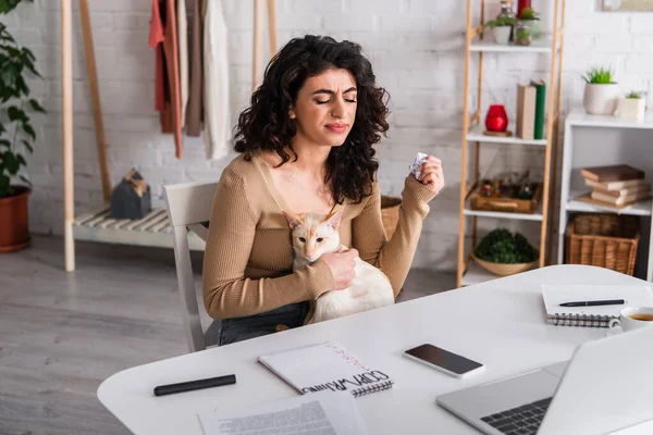 Upset copywriter holding paper and oriental cat near gadgets at home — Stock Photo