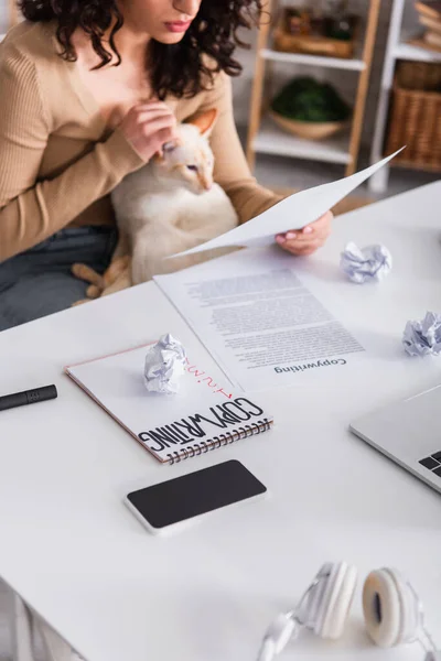 Vista recortada de dispositivos y papeles cerca de copywriter sosteniendo gato oriental en casa — Stock Photo