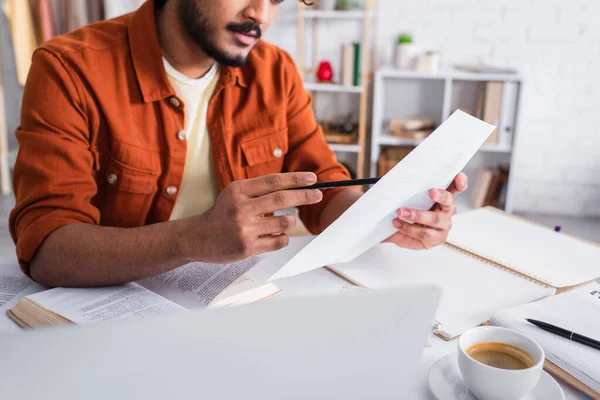 Cropped view of copywriter holding paper near notebooks and laptop at home — Stock Photo