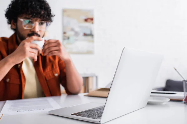 Laptop near blurred indian copywriter with cup at home — Stock Photo
