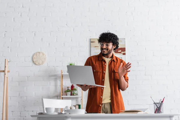 Cheerful indian freelancer having video chat on laptop in living room — Foto stock