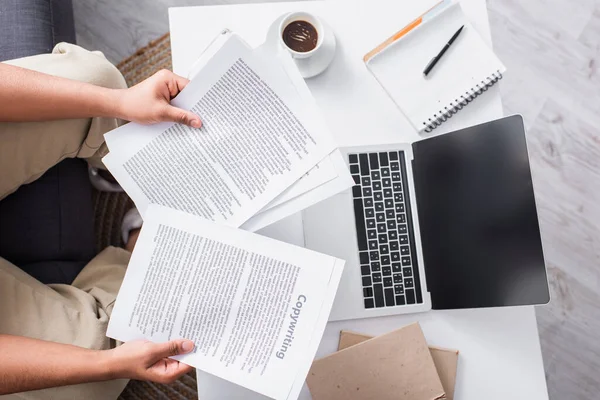 Top view of copywriter holding papers near laptop and coffee at home — Stock Photo