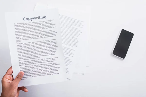 Top view of man holding paper with copywriting lettering near cellphone on table — Stock Photo