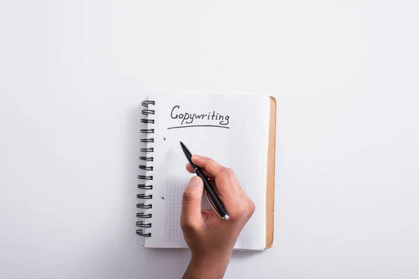 Top view of man holding pen near notebook with copywriting lettering on table — Stock Photo