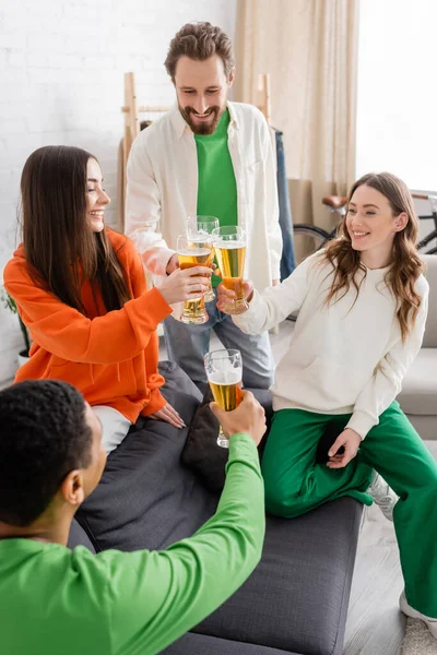 Fröhliche multiethnische Freunde, die im Wohnzimmer auf ein Glas Bier anstoßen — Stockfoto