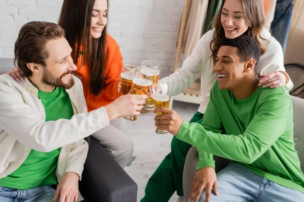 Cheerful and multicultural group of friends toasting glasses of beer in living room — Stock Photo