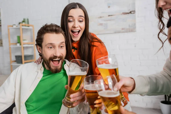 Amazed group of friends toasting glasses of beer in living room — Stock Photo