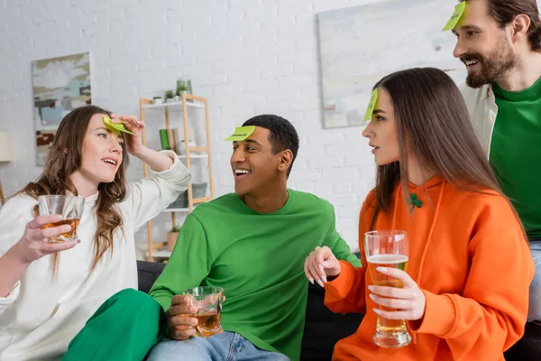 Interracial friends with sticky notes on foreheads playing guess who game on Saint Patrick Day — Stock Photo